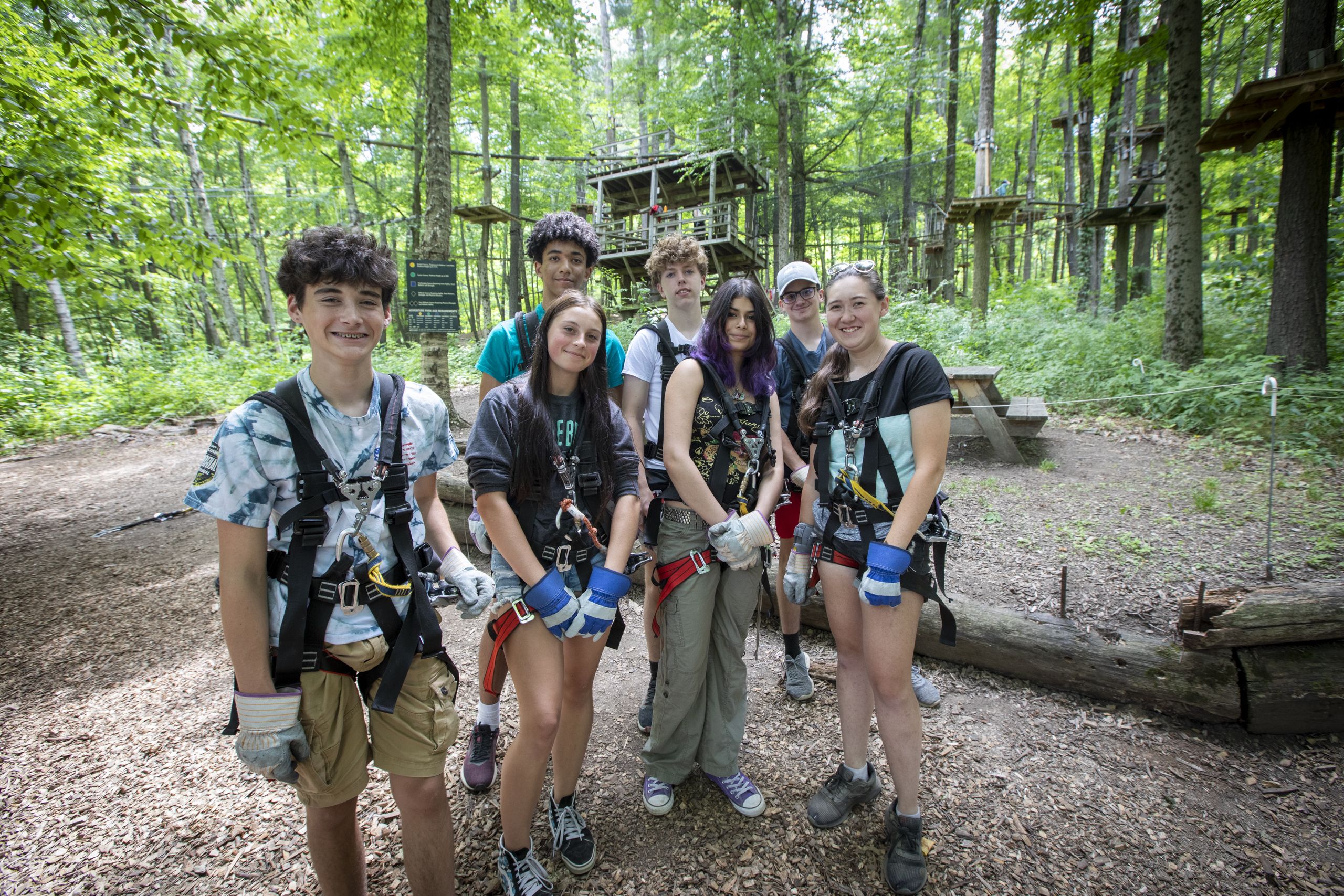 A group of high school kids wearing harnesses and smiling in front of the aerial adventure park at Catamount Resort