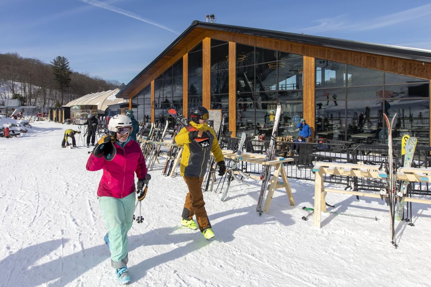 A woman and man walking in front of the Catamount Lodge with their skis
